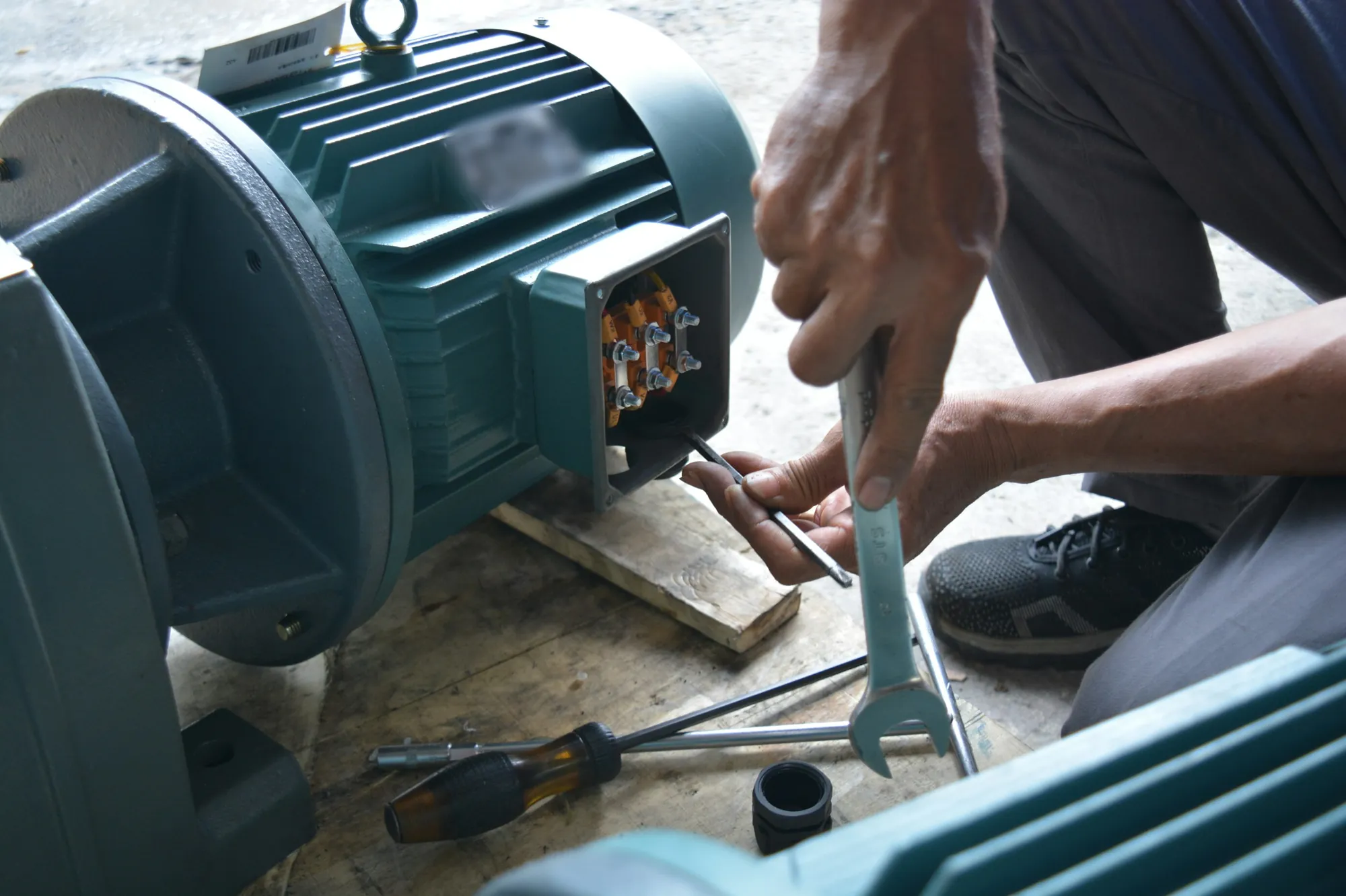 Technician working on a teal industrial motor terminal box